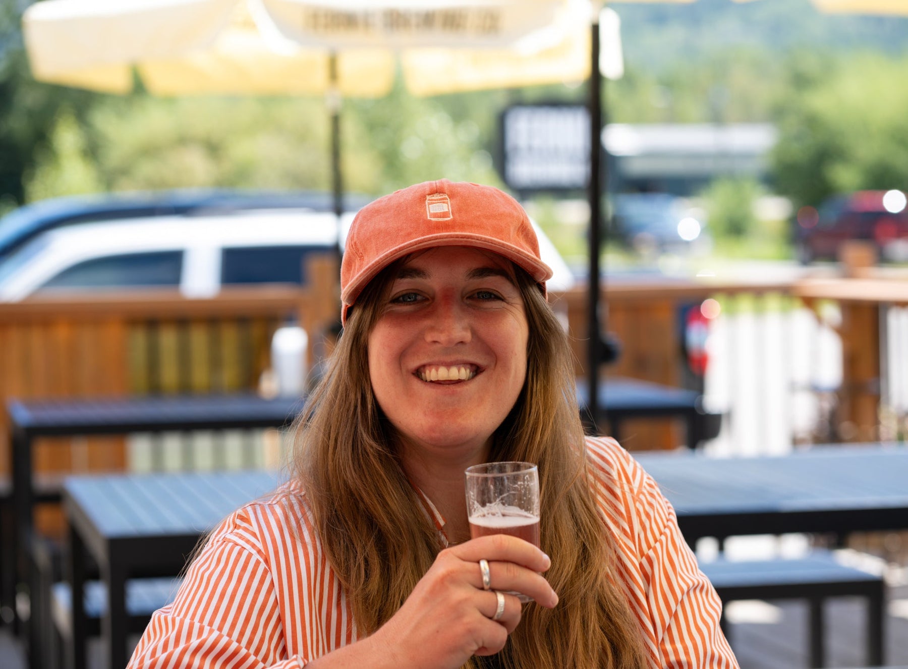A woman holding a glass of beer sitting on a patio in summer.